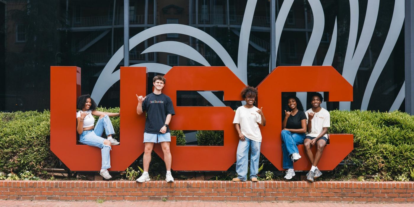 VERVE Columbia five college students pose in front of large red USC letters outside a building with glass windows.