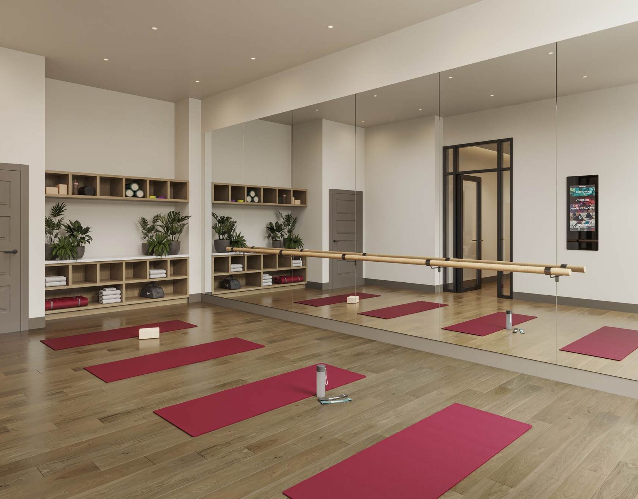 Yoga and barre studio at VERVE Columbia featuring mirrored walls, wooden floors, red yoga mats, wall-mounted screens, and built-in cubbies with towels, blocks, and greenery for a calm, focused workout environment.