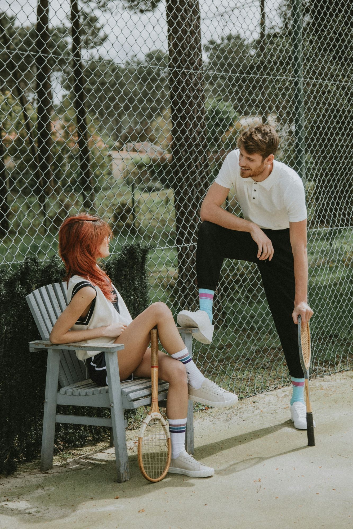 Two people relaxing by a tennis court at VERVE Columbia—one seated with a racket, the other standing with a paddle—dressed in sporty, casual attire.