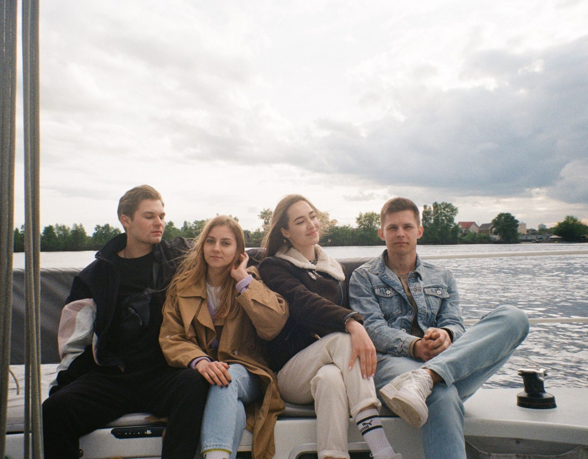 Group of four college friends sitting on a boat in jackets