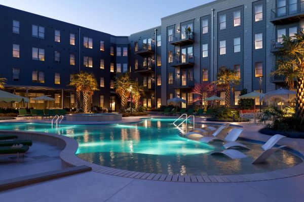 Resort-style pool at VERVE Columbia surrounded by lounge seating, palm trees, and modern apartment buildings, illuminated for a vibrant evening atmosphere.