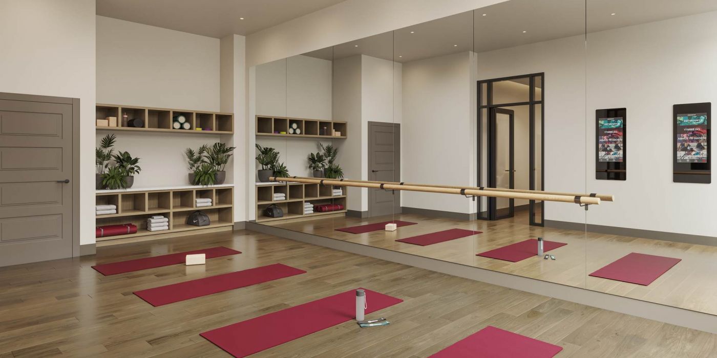 Yoga and barre studio at VERVE Columbia featuring mirrored walls, wooden floors, red yoga mats, wall-mounted screens, and built-in cubbies with towels, blocks, and greenery for a calm, focused workout environment.
