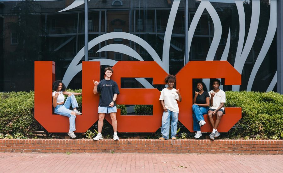 VERVE Columbia five college students pose in front of large red USC letters outside a building with glass windows.