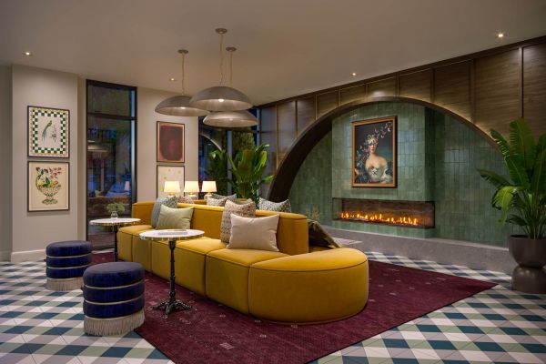 Lobby lounge at VERVE Columbia with a curved yellow sectional sofa, emerald green fireplace wall, modern lighting, and a portrait painting creating a cozy yet upscale ambiance.
