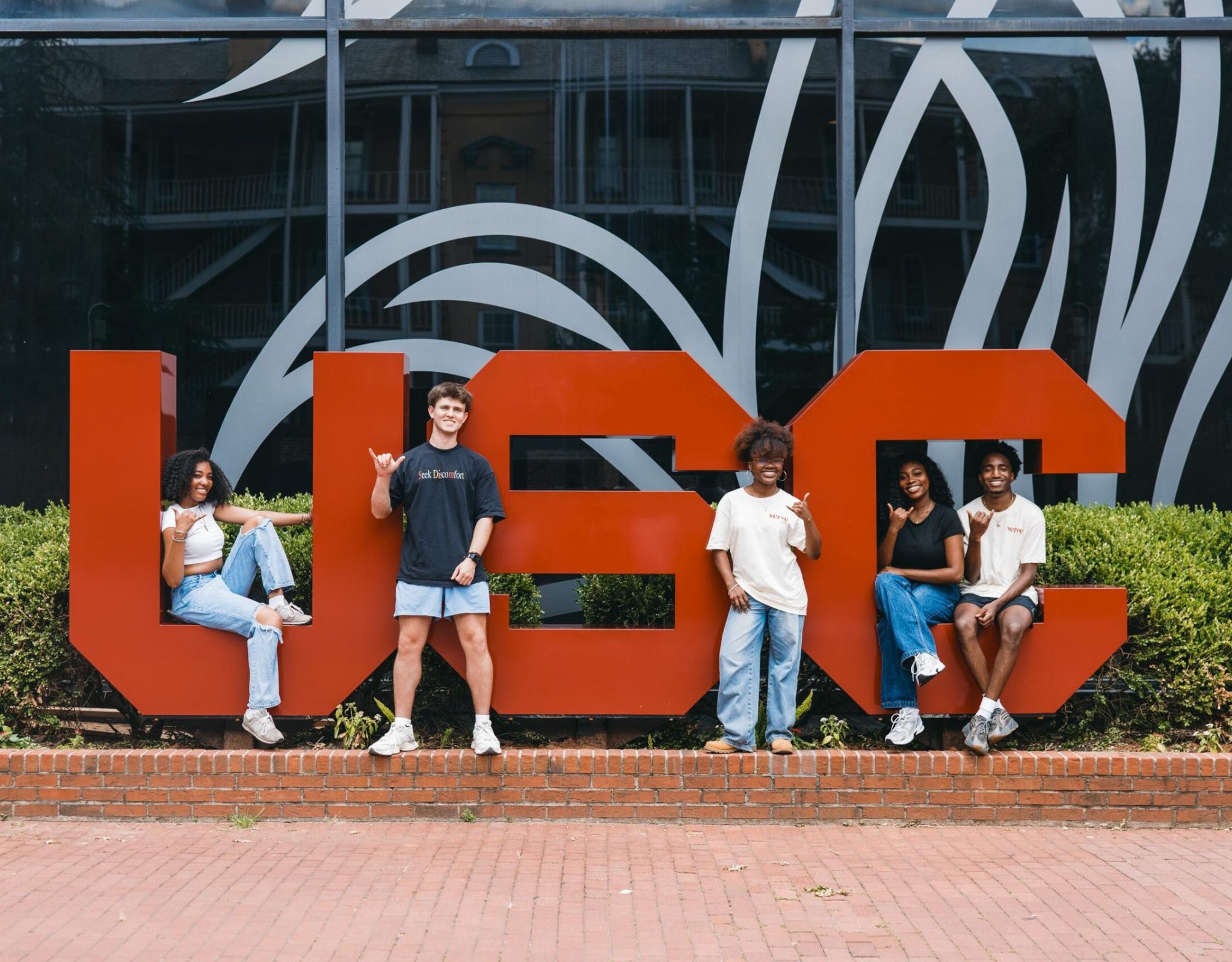 VERVE Columbia five college students pose in front of large red USC letters outside a building with glass windows.